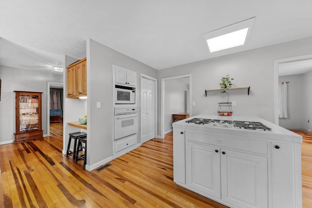 kitchen featuring white appliances, light hardwood / wood-style floors, and white cabinetry