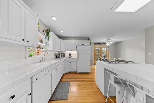 kitchen with tile countertops, white appliances, sink, light hardwood / wood-style floors, and white cabinetry