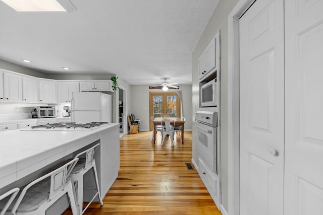 kitchen featuring appliances with stainless steel finishes, french doors, ceiling fan, white cabinets, and light hardwood / wood-style floors