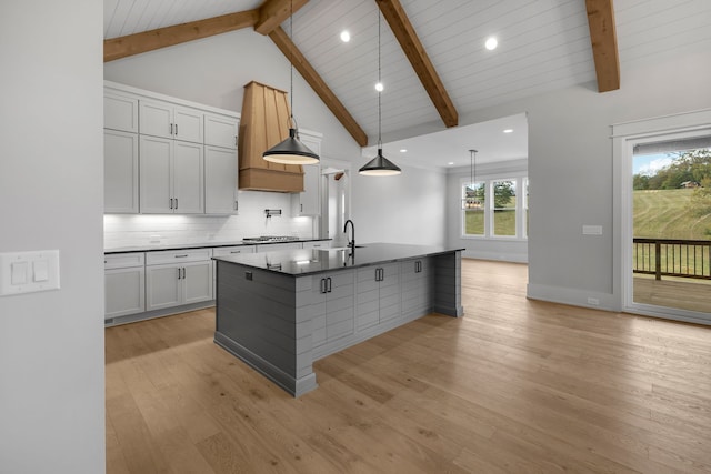 kitchen with beamed ceiling, backsplash, an island with sink, light hardwood / wood-style floors, and white cabinets