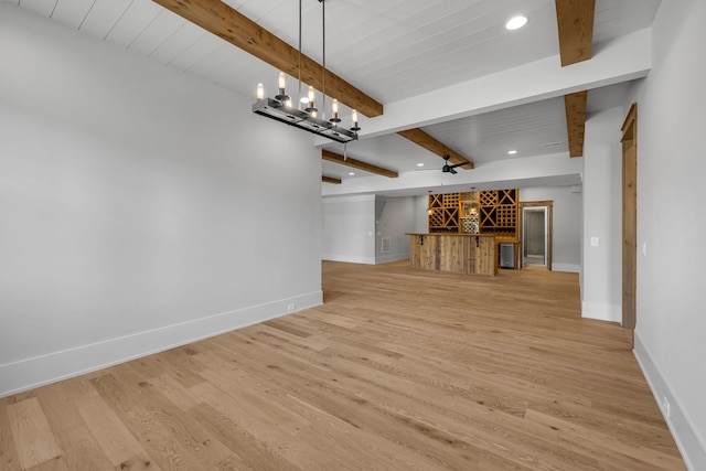 unfurnished living room featuring indoor bar, light hardwood / wood-style flooring, wooden ceiling, a notable chandelier, and beamed ceiling