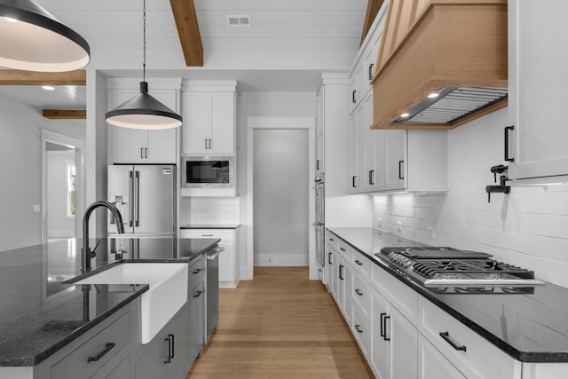 kitchen featuring white cabinets, custom exhaust hood, stainless steel appliances, and an island with sink