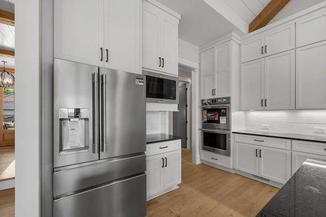 kitchen with appliances with stainless steel finishes, backsplash, white cabinets, vaulted ceiling with beams, and light hardwood / wood-style floors