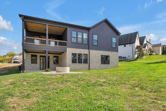 back of property with ceiling fan, a balcony, and a yard