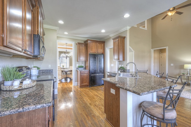 kitchen with sink, dark stone counters, black appliances, ceiling fan with notable chandelier, and ornamental molding