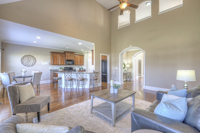 living room with ceiling fan, wood-type flooring, ornamental molding, and a high ceiling