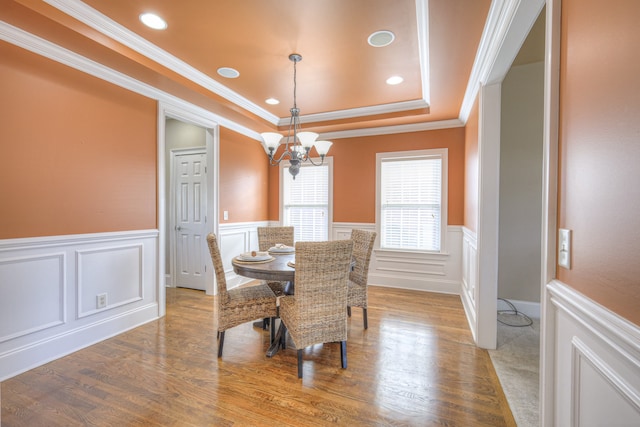 dining room with wood-type flooring, an inviting chandelier, a raised ceiling, and ornamental molding