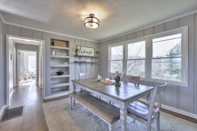 dining area with built in shelves, a textured ceiling, light hardwood / wood-style flooring, and crown molding