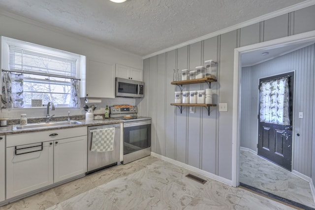 kitchen with white cabinets, crown molding, sink, a textured ceiling, and stainless steel appliances