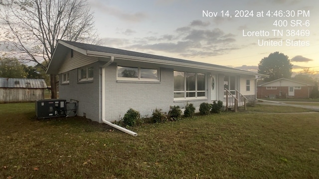 property exterior at dusk featuring a lawn and cooling unit