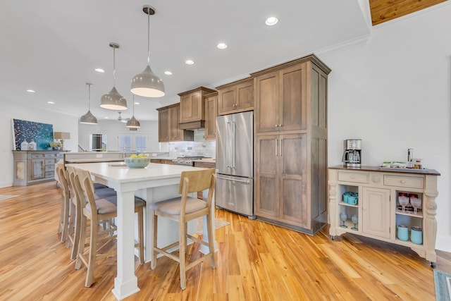 kitchen with stainless steel appliances, a kitchen breakfast bar, light hardwood / wood-style flooring, crown molding, and pendant lighting