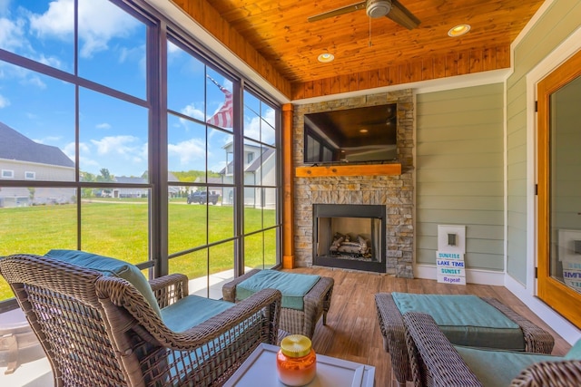 sunroom with plenty of natural light, ceiling fan, an outdoor stone fireplace, and wooden ceiling