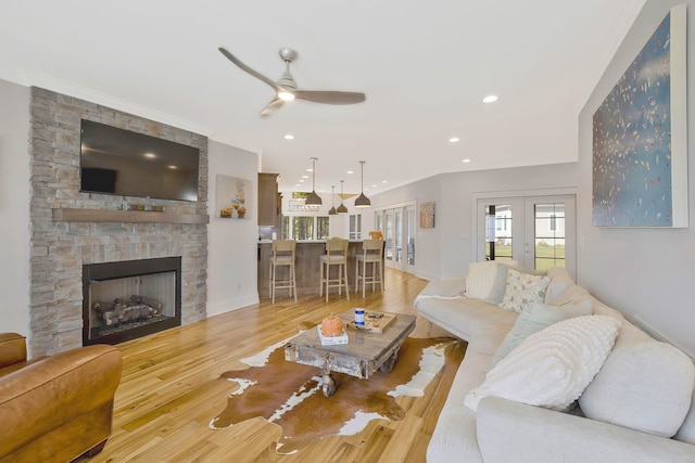 living room with a fireplace, ceiling fan, light hardwood / wood-style flooring, and french doors