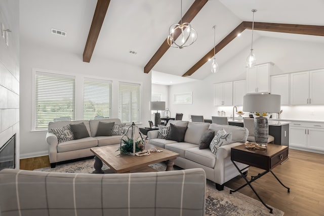 living room featuring sink, light hardwood / wood-style flooring, high vaulted ceiling, beamed ceiling, and a fireplace