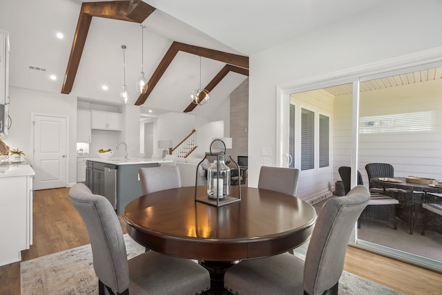 dining space featuring lofted ceiling with beams, sink, and light hardwood / wood-style flooring