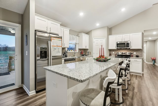 kitchen with white cabinetry, a kitchen island, stainless steel appliances, and vaulted ceiling