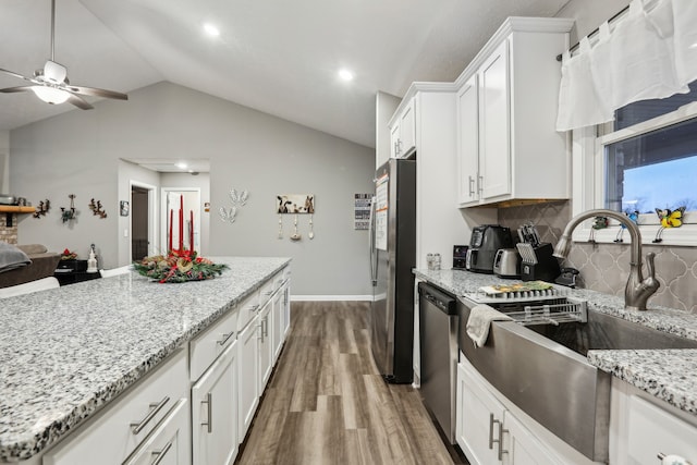 kitchen with decorative backsplash, appliances with stainless steel finishes, hardwood / wood-style floors, white cabinetry, and lofted ceiling