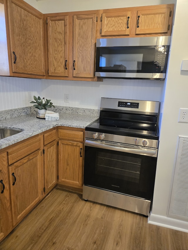 kitchen with sink, light stone countertops, light wood-type flooring, and stainless steel appliances