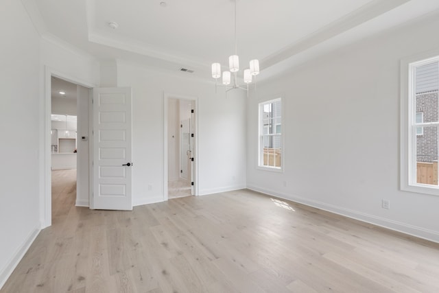 spare room featuring a tray ceiling, light hardwood / wood-style flooring, ornamental molding, and an inviting chandelier