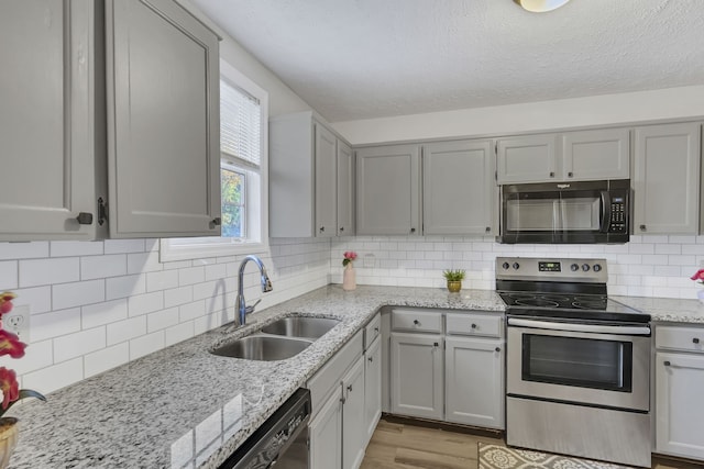 kitchen with appliances with stainless steel finishes, backsplash, sink, gray cabinets, and light hardwood / wood-style floors