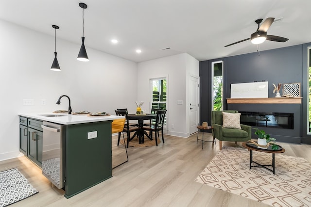 kitchen featuring kitchen peninsula, stainless steel dishwasher, sink, pendant lighting, and light hardwood / wood-style flooring