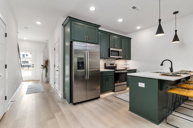 kitchen with a kitchen breakfast bar, green cabinets, decorative light fixtures, appliances with stainless steel finishes, and light wood-type flooring