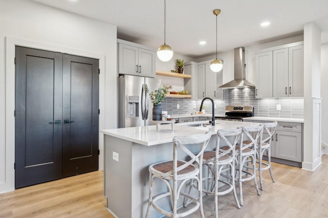 kitchen featuring appliances with stainless steel finishes, wall chimney exhaust hood, an island with sink, sink, and hanging light fixtures