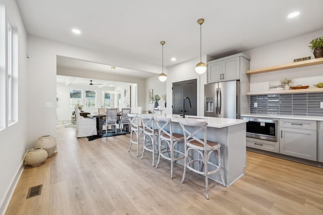 kitchen featuring gray cabinetry, decorative light fixtures, a center island with sink, and appliances with stainless steel finishes