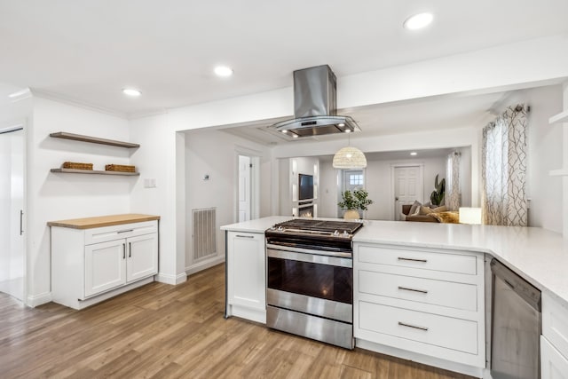 kitchen featuring hanging light fixtures, kitchen peninsula, appliances with stainless steel finishes, island range hood, and white cabinetry