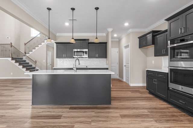 kitchen with a center island with sink, hanging light fixtures, sink, hardwood / wood-style flooring, and appliances with stainless steel finishes