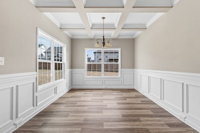 unfurnished dining area with beam ceiling, an inviting chandelier, ornamental molding, and light wood-type flooring