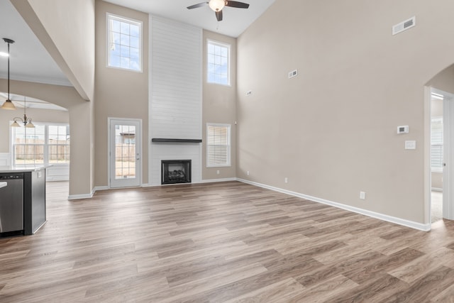 unfurnished living room with a fireplace, a high ceiling, light wood-type flooring, and ceiling fan