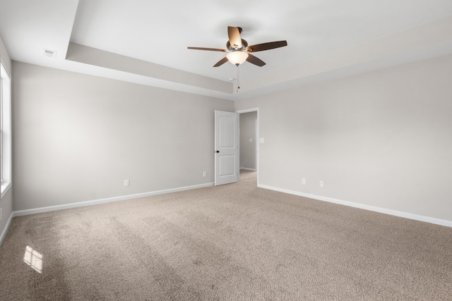 empty room featuring a raised ceiling, ceiling fan, and carpet