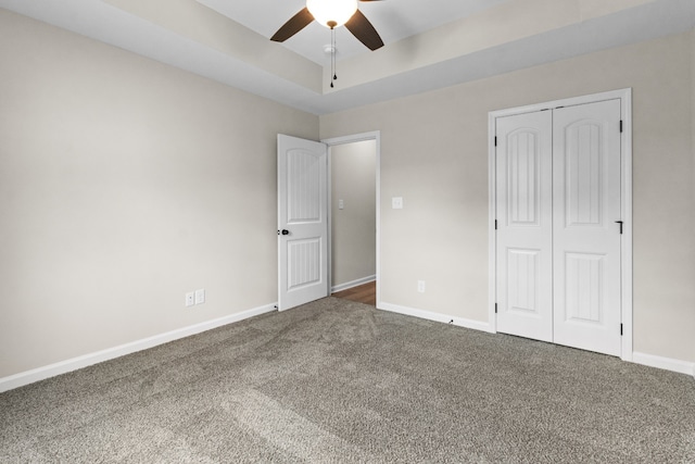 unfurnished bedroom with ceiling fan, a closet, and dark colored carpet