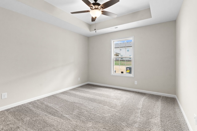 carpeted empty room with ceiling fan and a raised ceiling