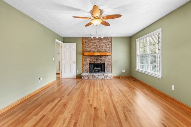 unfurnished living room with a stone fireplace, ceiling fan, light hardwood / wood-style flooring, and a textured ceiling