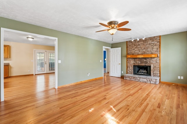 unfurnished living room with light wood-type flooring, track lighting, a textured ceiling, ceiling fan, and a stone fireplace