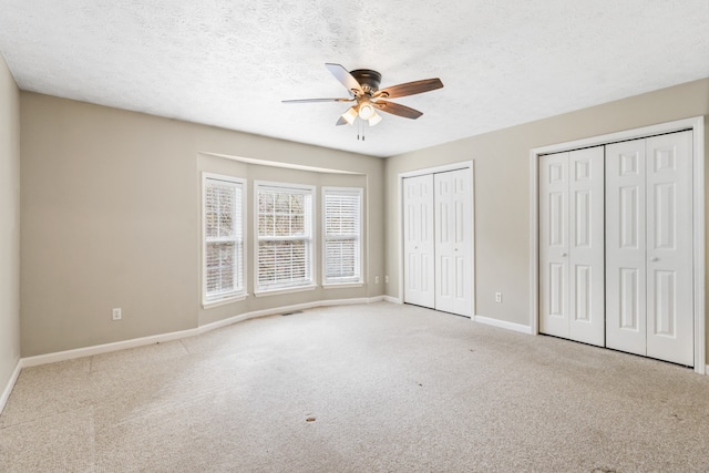 unfurnished bedroom featuring ceiling fan, light colored carpet, a textured ceiling, and multiple closets