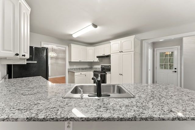 kitchen featuring electric range, sink, light stone countertops, black fridge, and white cabinets