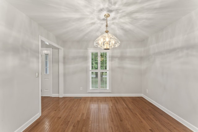 empty room with hardwood / wood-style floors and a notable chandelier