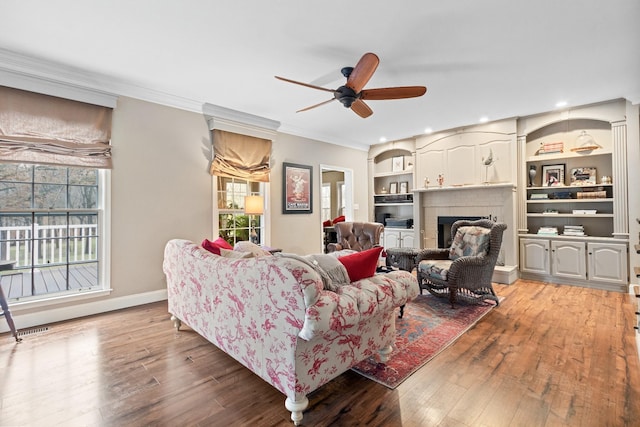 living room featuring hardwood / wood-style floors, ceiling fan, ornamental molding, and a fireplace