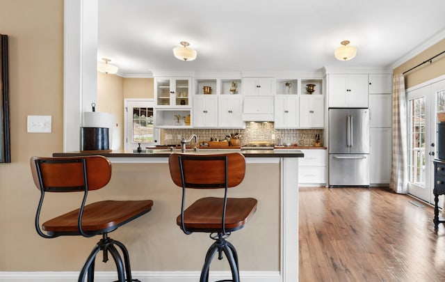 kitchen with white cabinets, a breakfast bar, stainless steel fridge, and kitchen peninsula