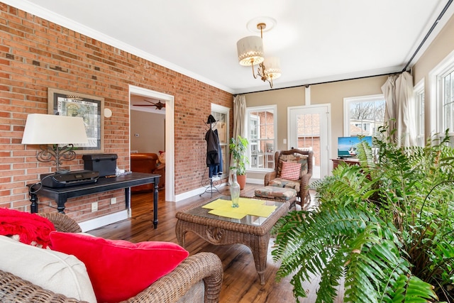 living room featuring crown molding, brick wall, ceiling fan with notable chandelier, and hardwood / wood-style flooring