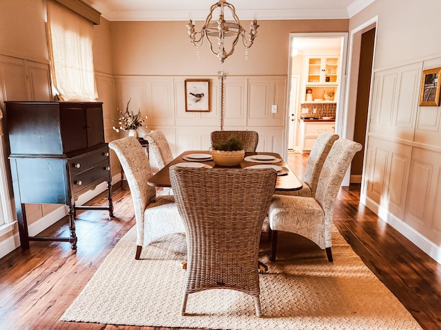 dining area with a decorative wall, hardwood / wood-style floors, a chandelier, a wainscoted wall, and ornamental molding