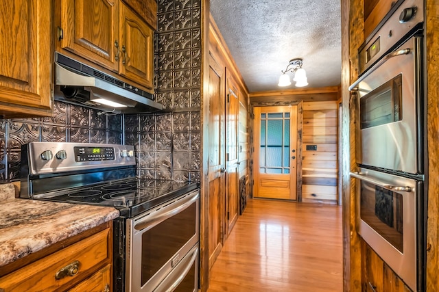 kitchen with light stone countertops, wood walls, a textured ceiling, appliances with stainless steel finishes, and light wood-type flooring