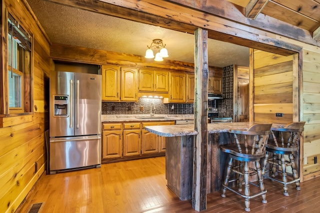 kitchen featuring a breakfast bar area, wood walls, light hardwood / wood-style floors, and stainless steel refrigerator with ice dispenser