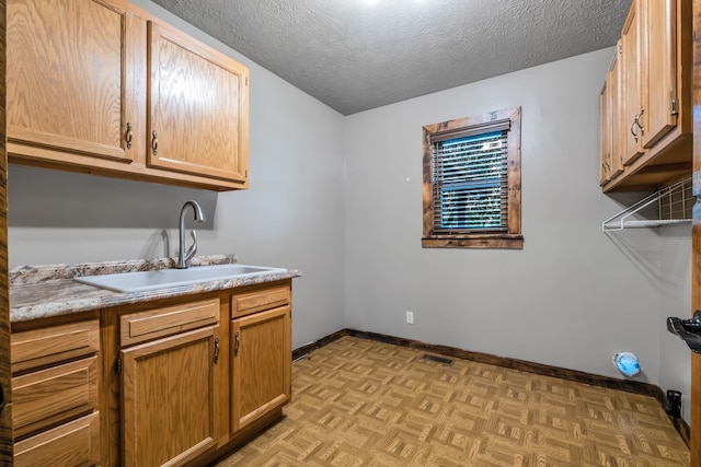 laundry area featuring a textured ceiling, sink, and light parquet flooring