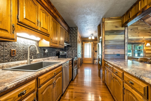 kitchen with appliances with stainless steel finishes, sink, hardwood / wood-style flooring, and wood walls