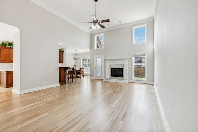 unfurnished living room featuring ceiling fan with notable chandelier, light wood-type flooring, a towering ceiling, and ornamental molding