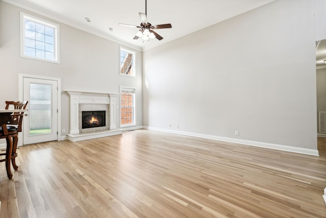 unfurnished living room featuring crown molding, plenty of natural light, a towering ceiling, and light wood-type flooring